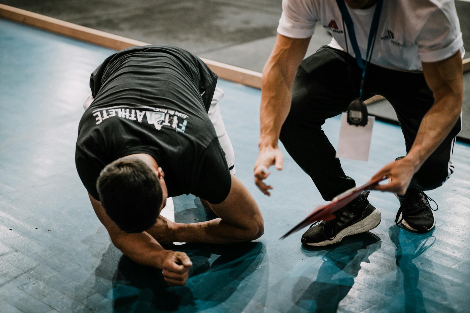An athlete being assisted by a coach during an indoor training session on a blue floor. (Photo by Ardit Mbrati on Pexels)