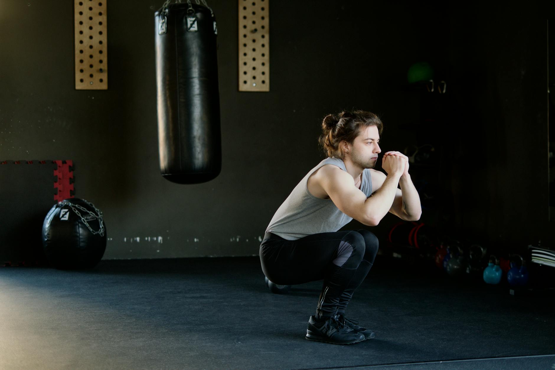 A man is doing squats in a gym with a punching bag. The setting appears stylish and focused on fi... (Photo by Ivan S on Pexels)