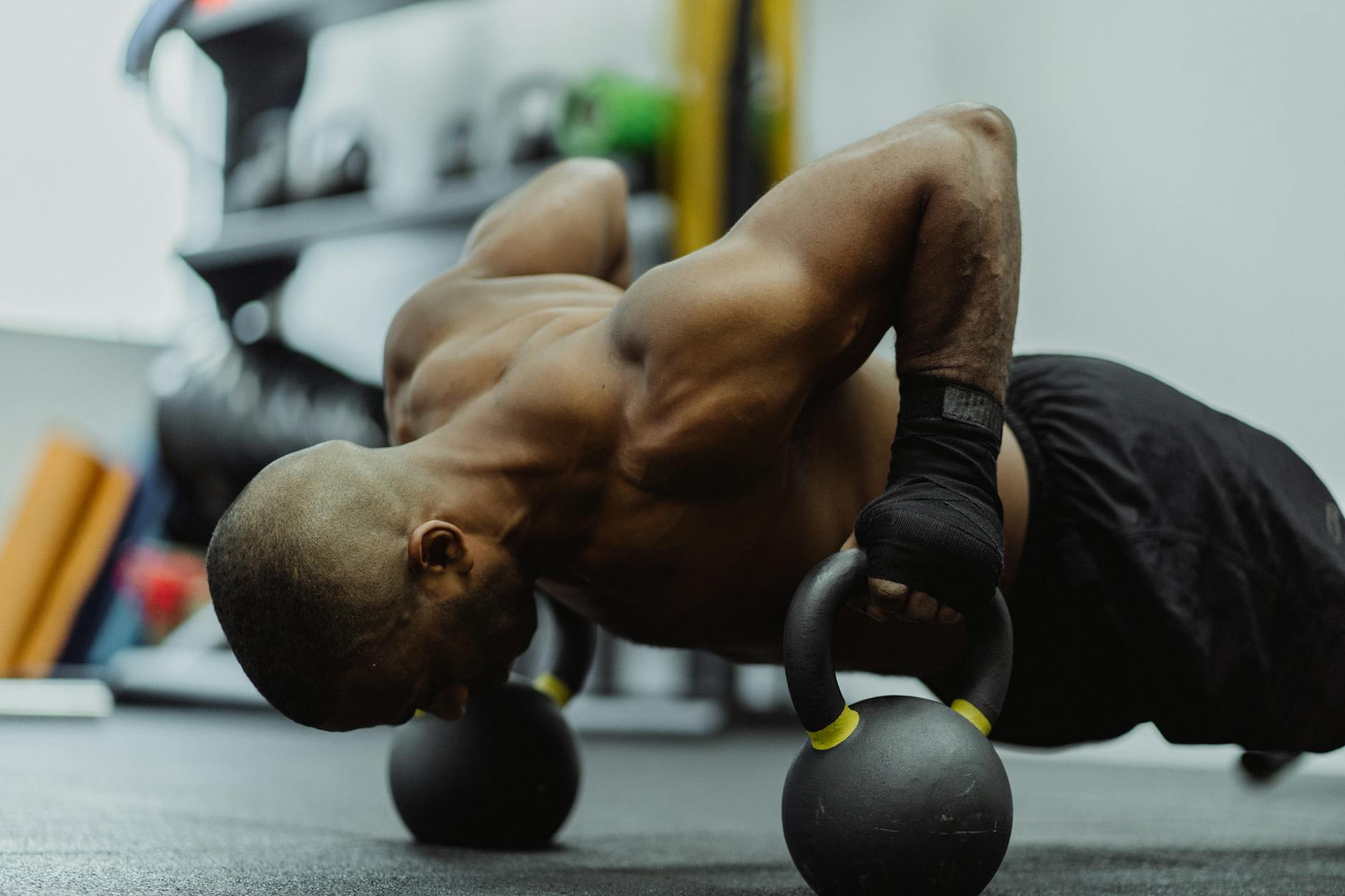 A shirtless man engages in intense kettlebell push-ups for strength and fitness. (Photo by Ketut Subiyanto on Pexels)