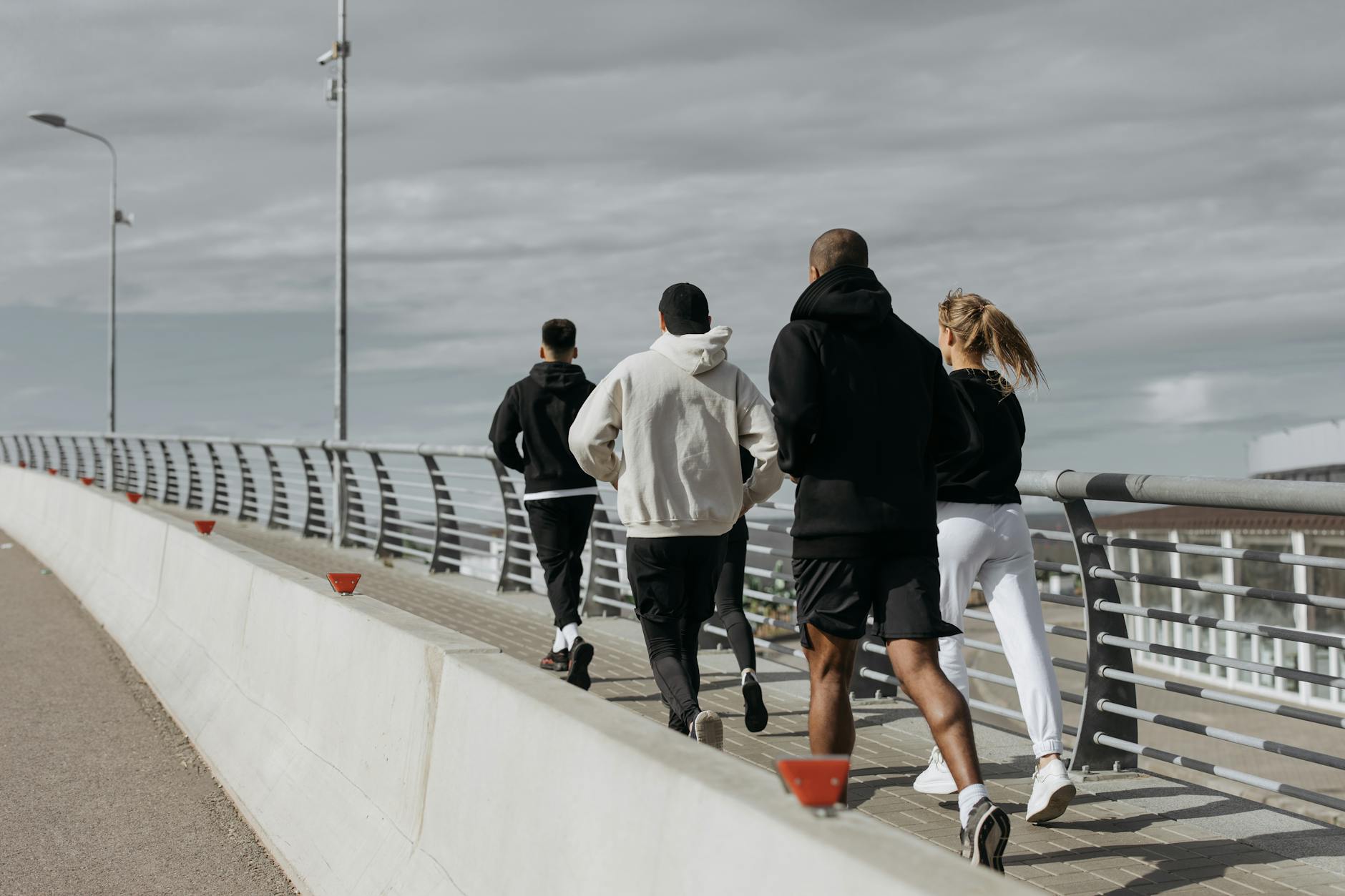 A diverse group of adults jogging together on a city bridge during the day. (Photo by cottonbro studio on Pexels)