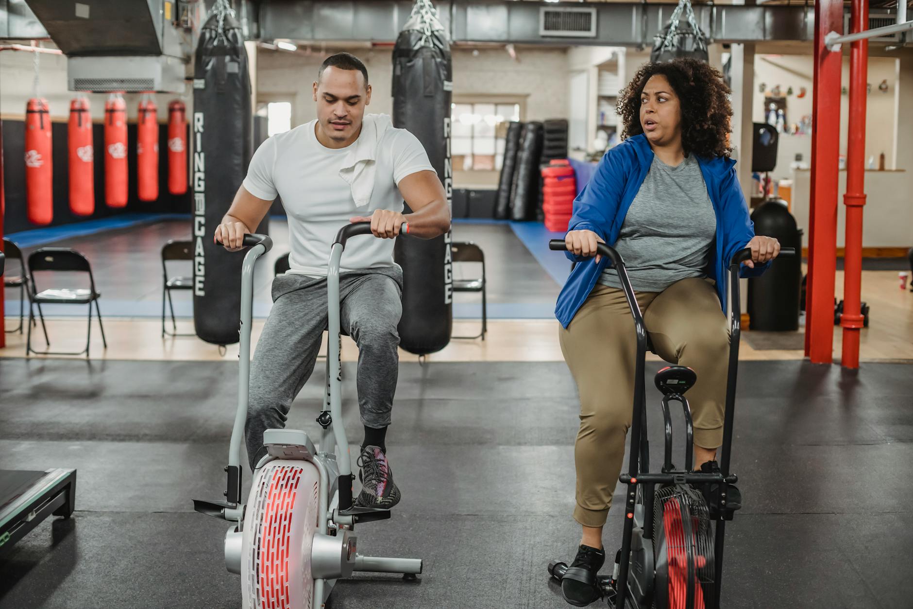 Full body of overweight black woman sitting on cycling machine and looking at fitness trainer (Photo by Julia Larson on Pexels)