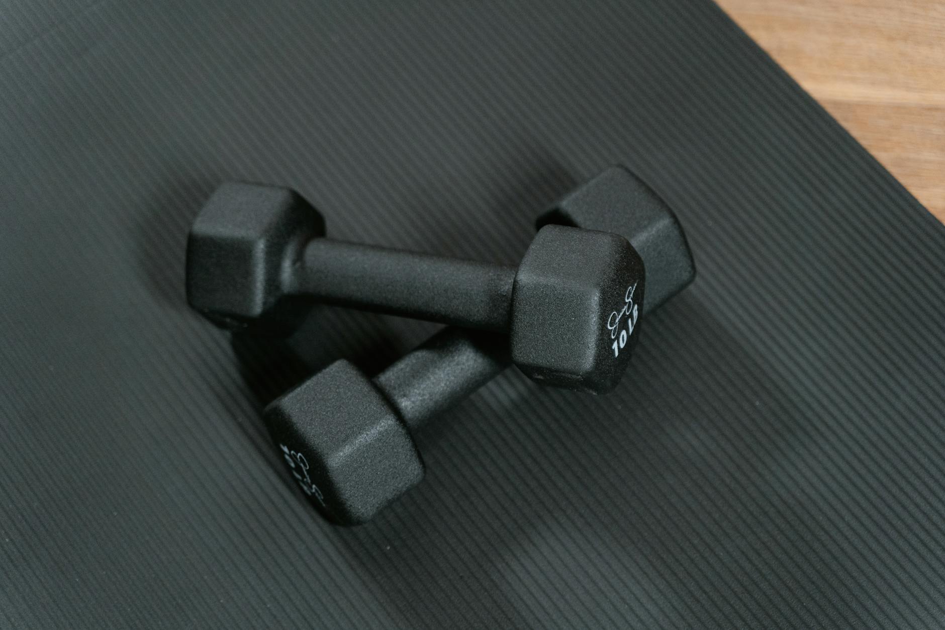 Black dumbbells placed on a yoga mat, perfect for home workouts and strength training. (Photo by MART  PRODUCTION on Pexels)