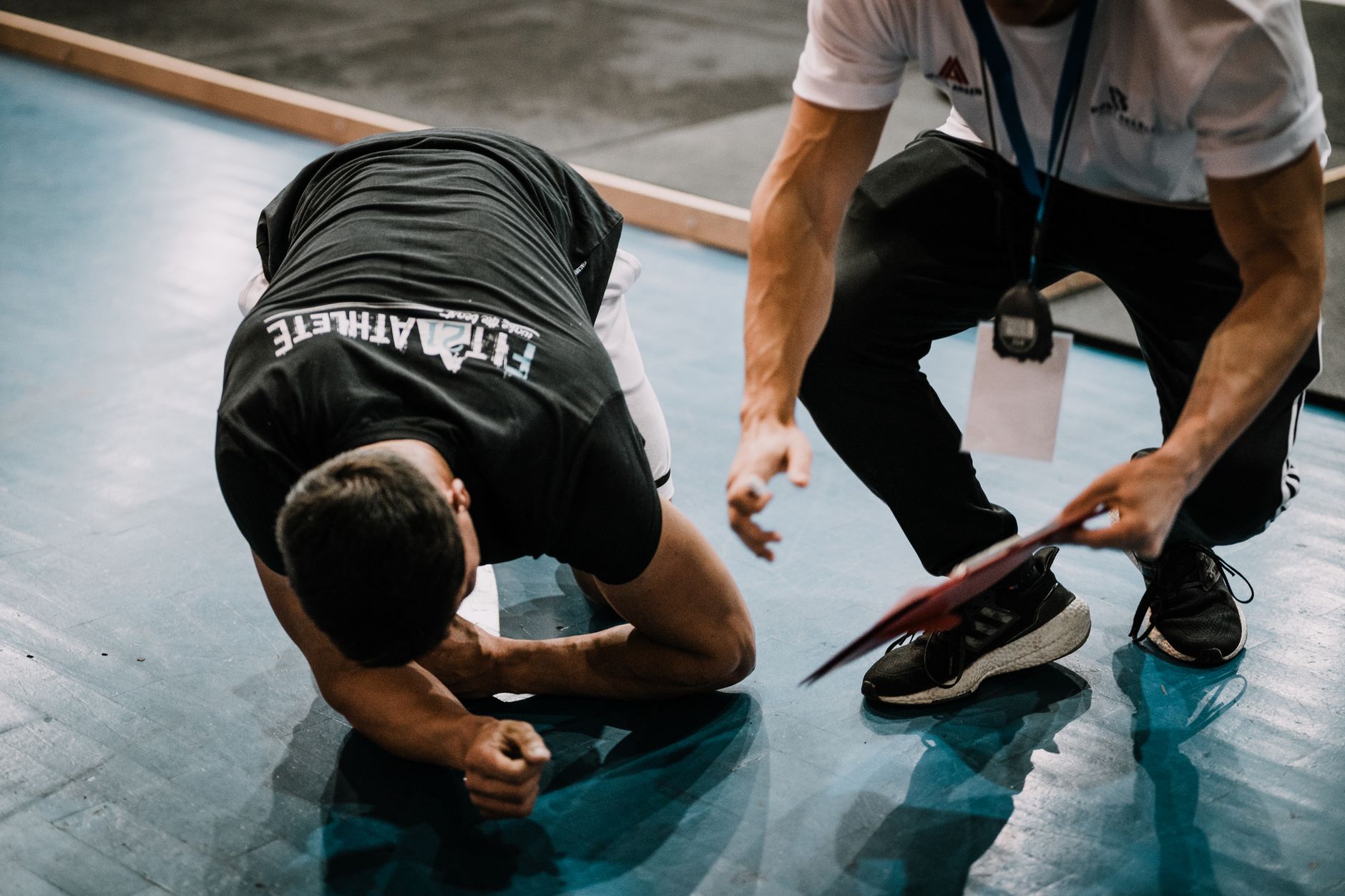 An athlete being assisted by a coach during an indoor training session on a blue floor. (Photo by Ardit Mbrati on Pexels)