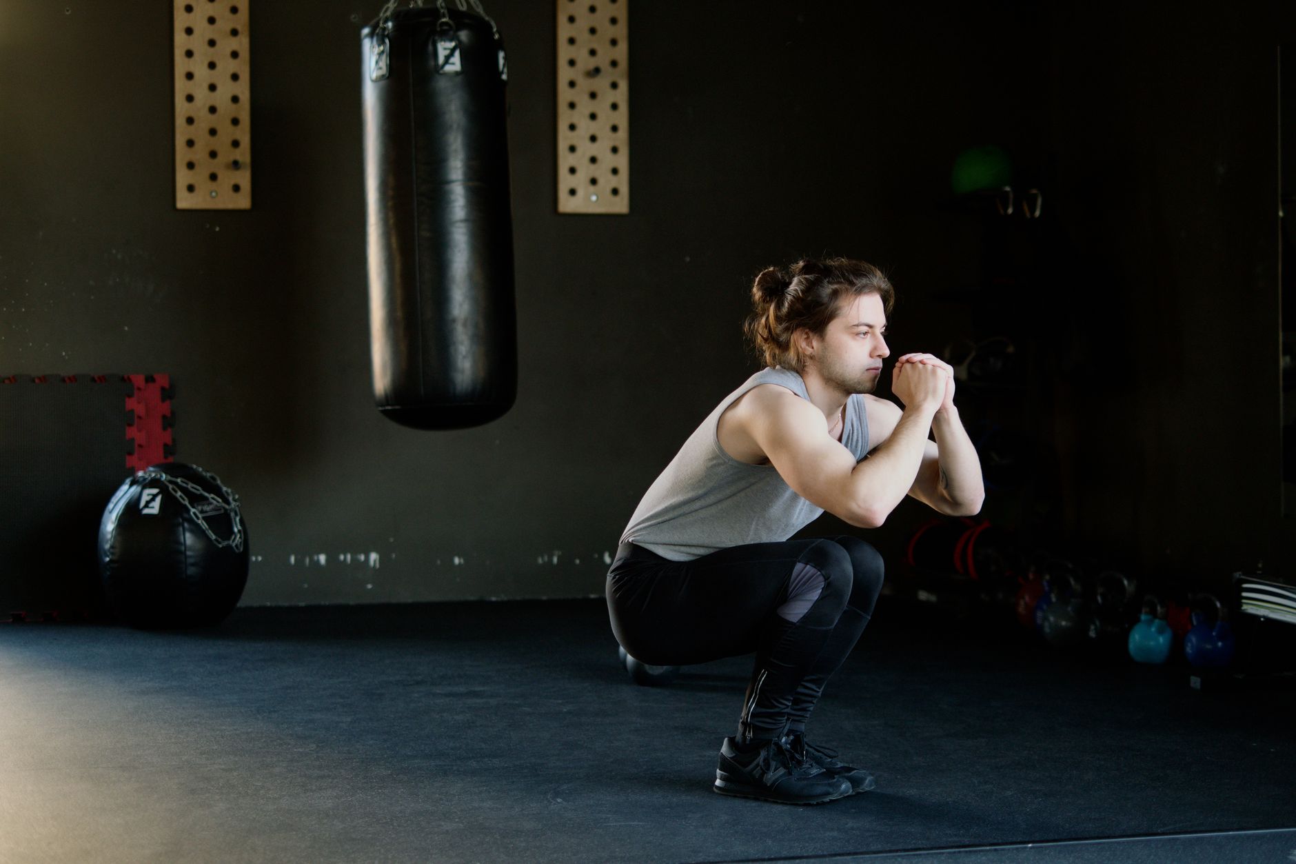 A man is doing squats in a gym with a punching bag. The setting appears stylish and focused on fi... (Photo by Ivan S on Pexels)