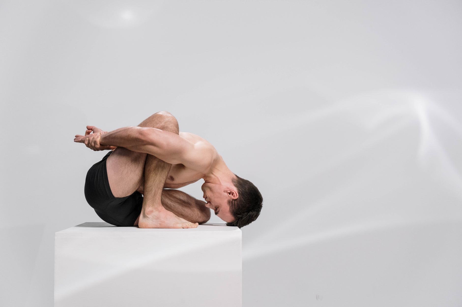 A highly flexible man demonstrates an advanced contortion pose on a white platform in a minimalis... (Photo by cottonbro studio on Pexels)